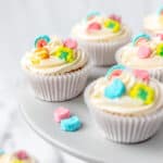 Five cupcakes in white cupcake papers with lucky charms marshmallows on top of the frosting.