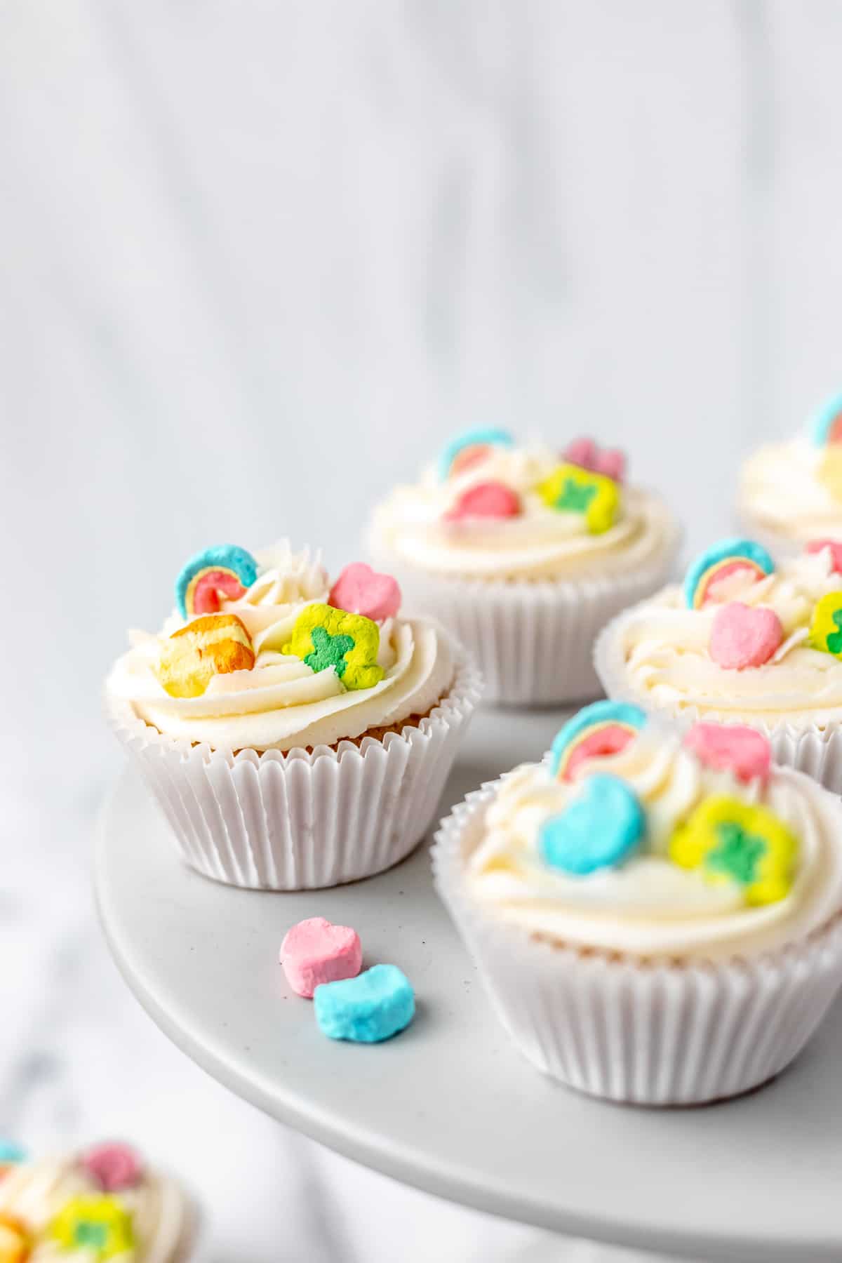 Lucky Charms cupcakes on a cake stand with extra marshmallows around them.