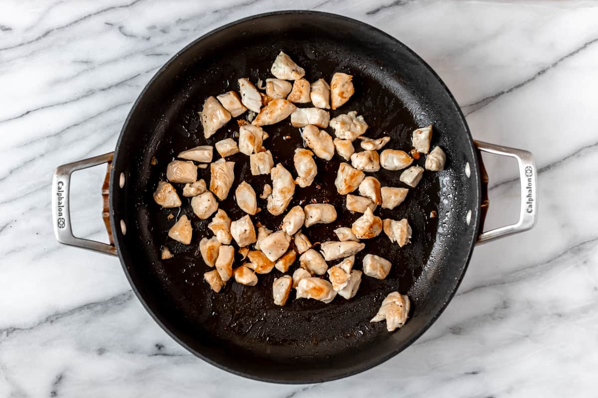 Chunks of chicken cooking in a black skillet.