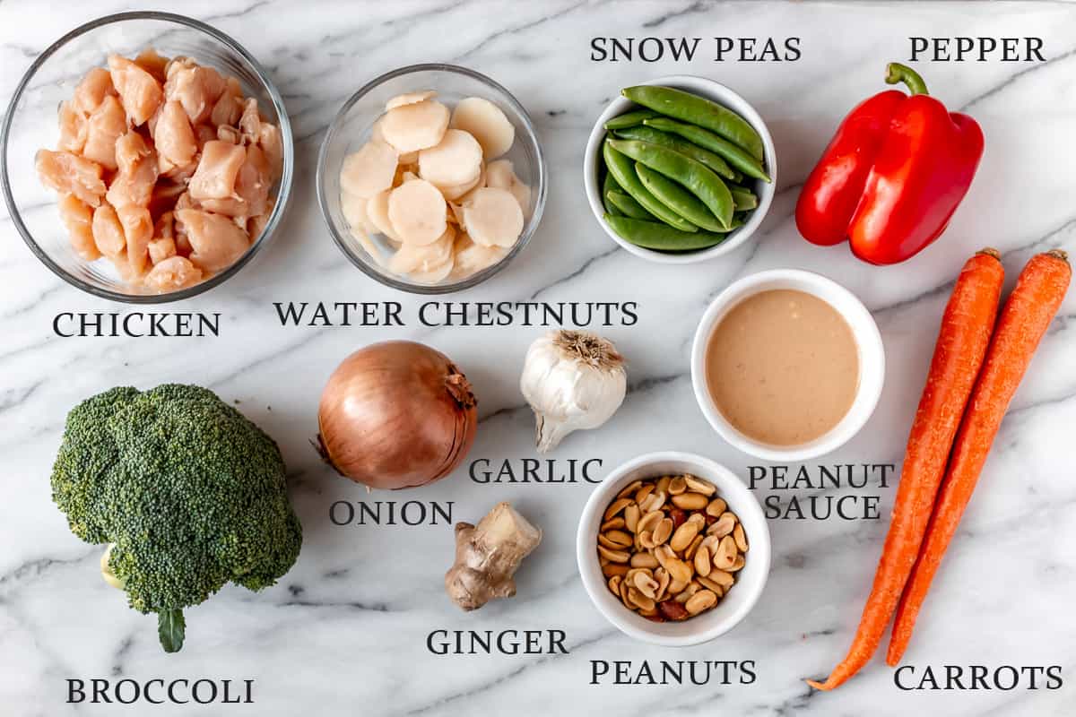 Ingredients needed to make chicken peanut stir fry on a marble background with text overlay.
