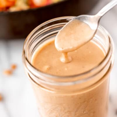 Peanut sauce on a spoon over a glass jar of more sauce.
