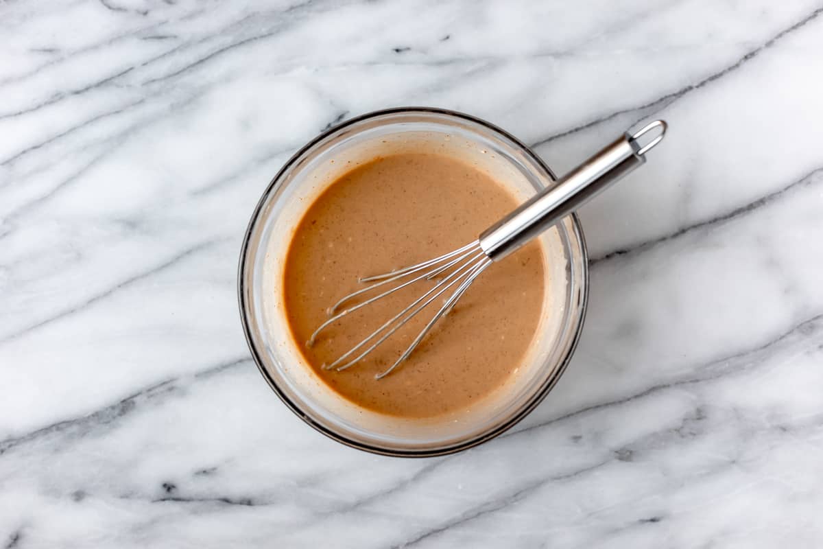 Peanut sauce in a glass bowl with a whisk on a marble background.