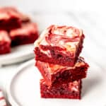 A stack of three red velvet cheesecake brownies on a plate with text overlay.