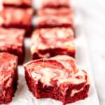 Red velvet cheesecake brownies on parchment paper with one turned and a bite taken out of it with text overlay.