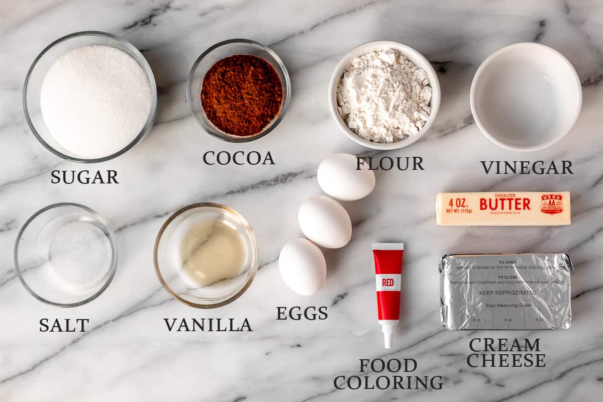 Ingredients needed to make red velvet brownies with a cheesecake swirl on a marble background with text overlay.