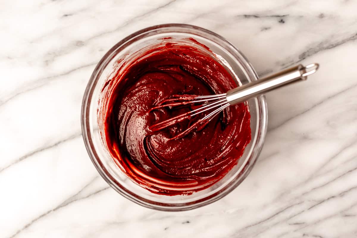 Red velvet brownie batter in a glass bowl with a whisk.