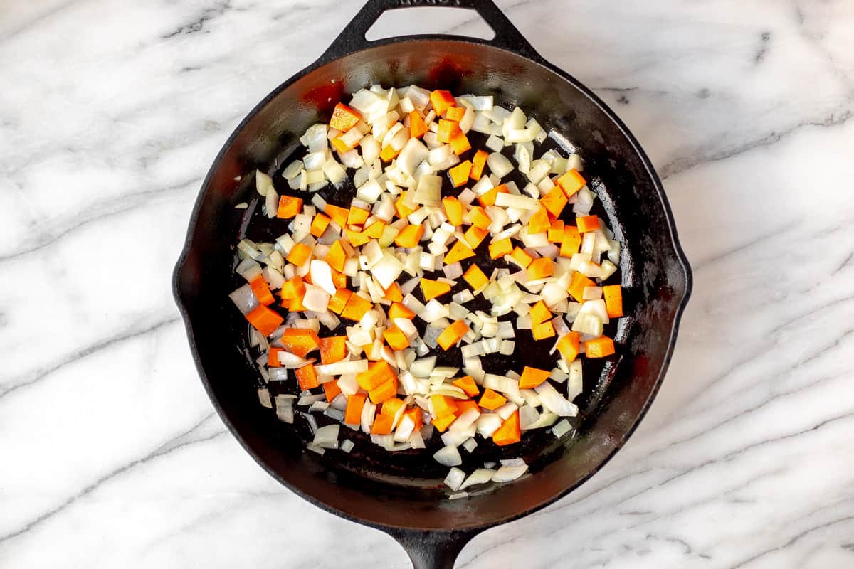 Diced onions and carrots cooking in a cast iron skillet.