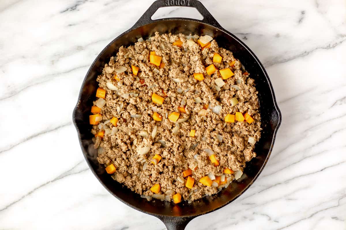 Ground beef, carrots, and onions cooking in a cast iron skillet.