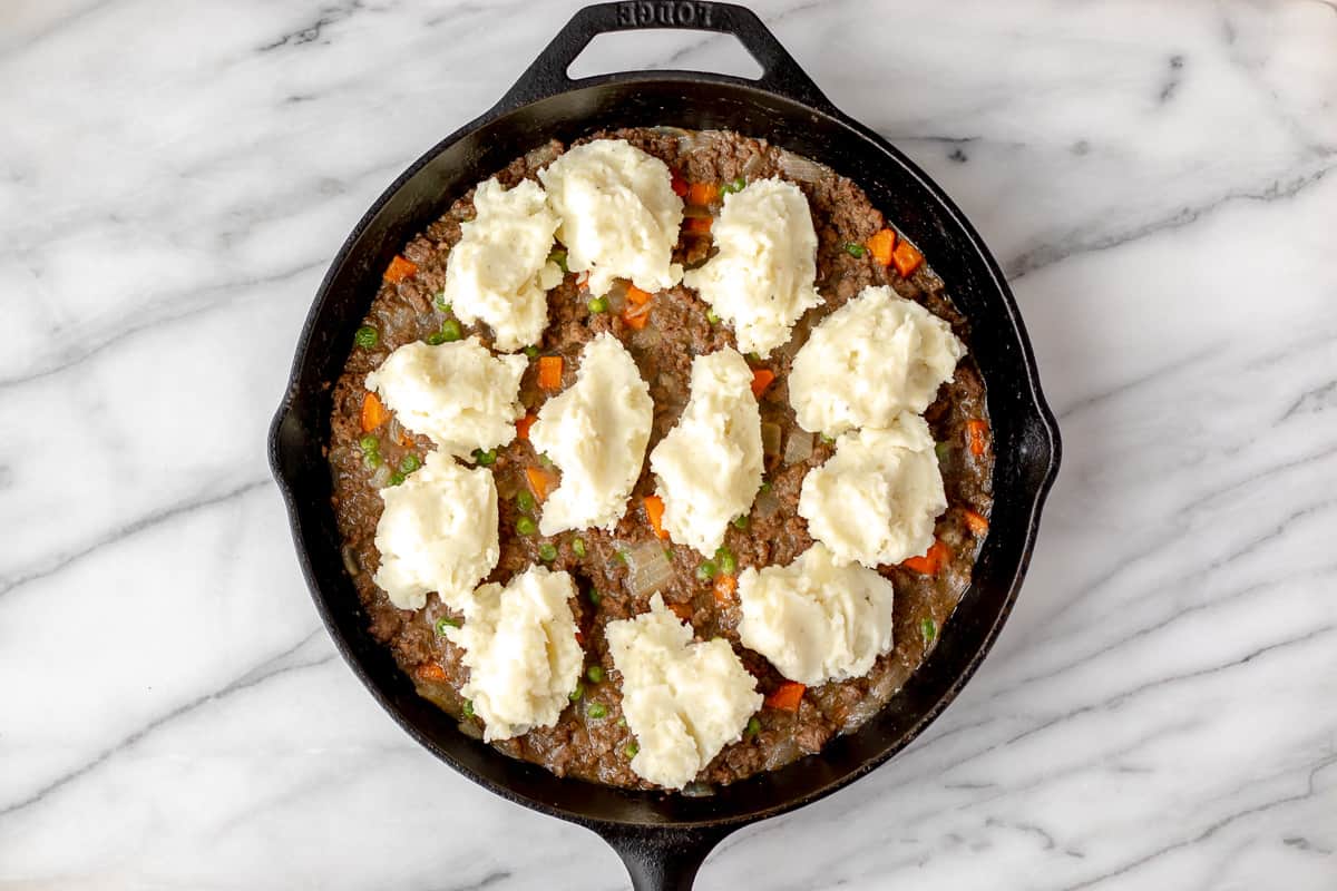 Mashed potatoes dolloped over a Shepherd's Pie filling in a cast iron skillet.