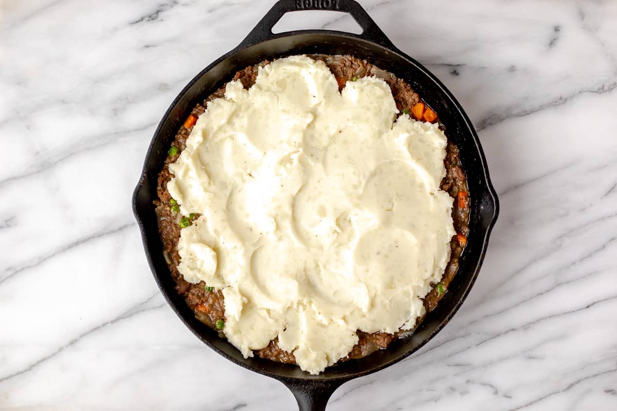 Mashed potatoes spread over a Shepherd's Pie filling in a cast iron skillet.