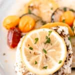 Baked cod and vegetables topped with lemon on a white plate with text overlay.