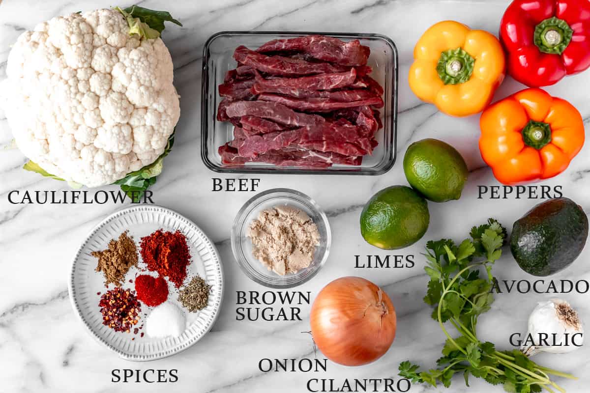 Ingredients needed to make beef fajita bowls on a marble background with text overlay.