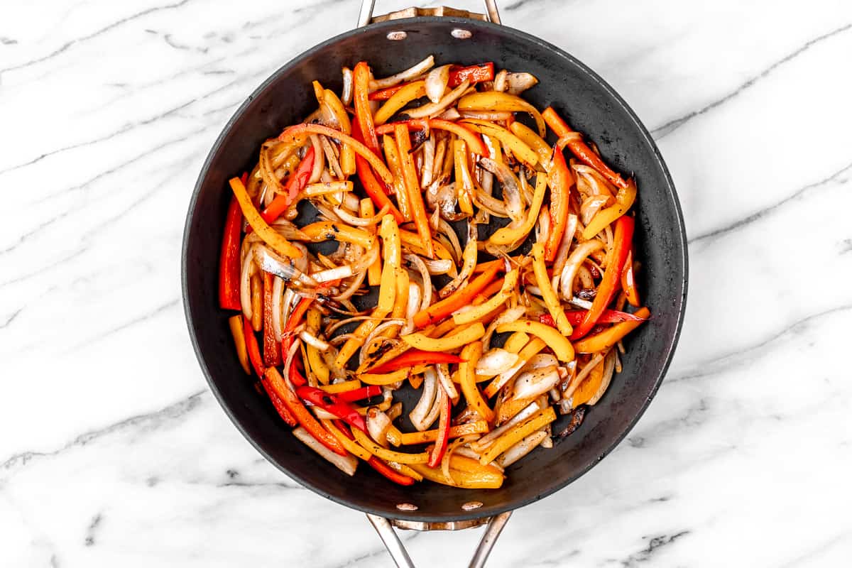 Onion and pepper strips cooking in a black skillet.