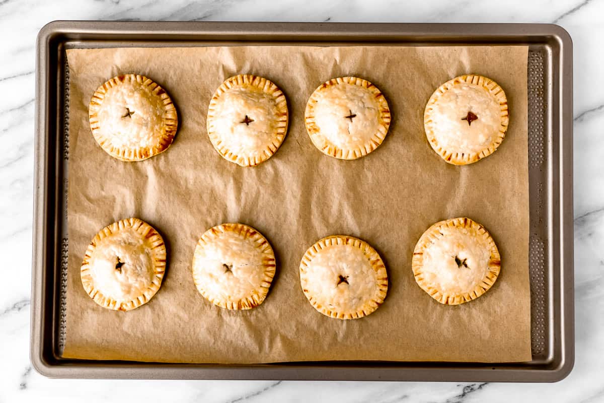 A parchment paper lined baking sheet with 8 baked hand pies on it.