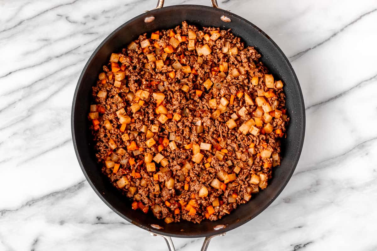 Ground beef, carrots and potatoes cooking in a back skillet.
