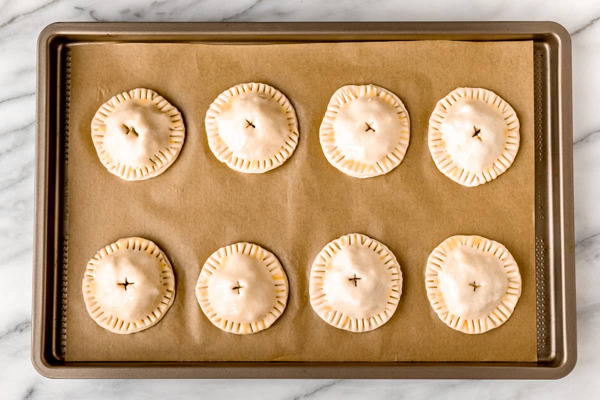 A parchment paper lined baking sheet with 8 hand pies on it.