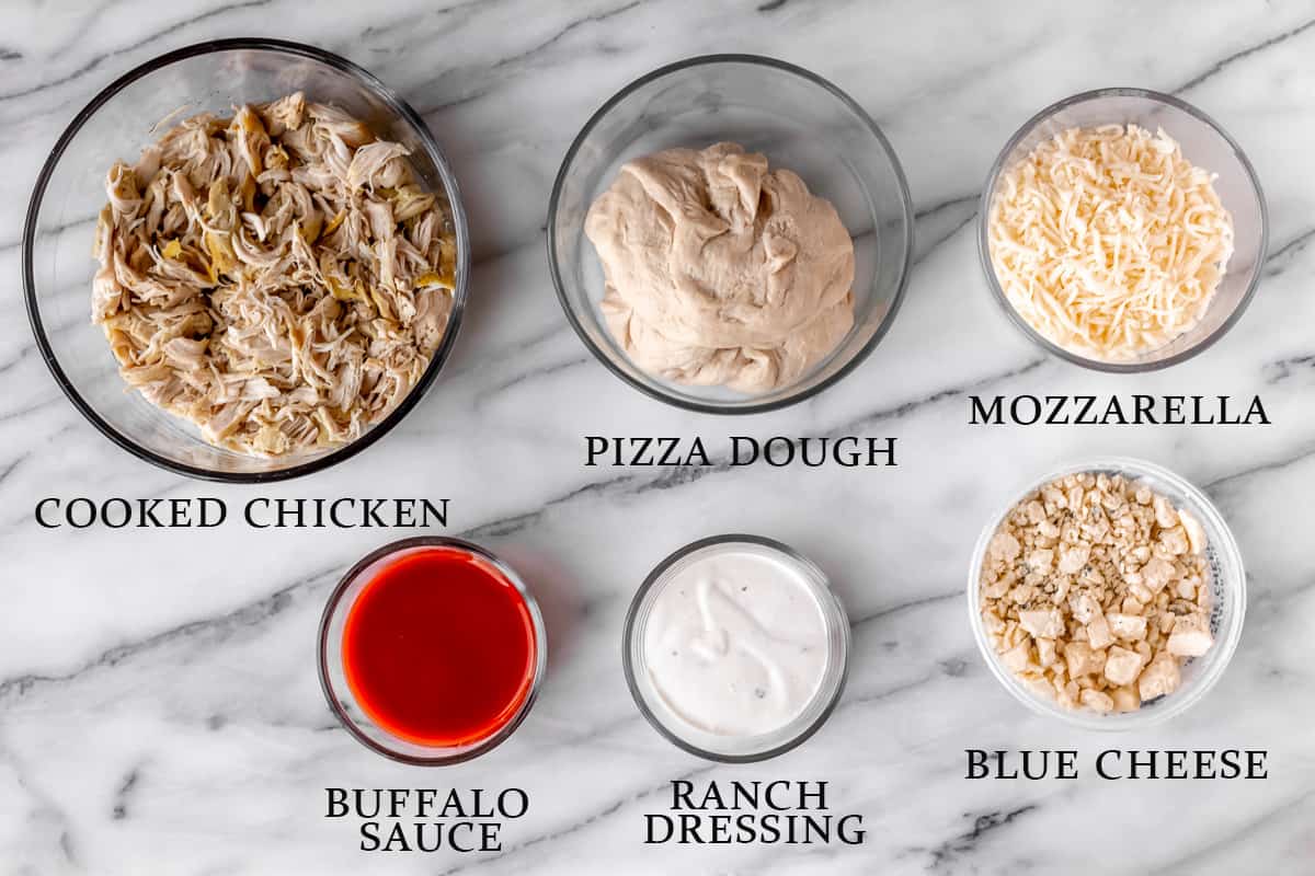 Ingredients needed to make a buffalo chicken pizza on a marble background with text overlay.