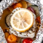 A cod fillet on vegetables topped with a lemon in foil.