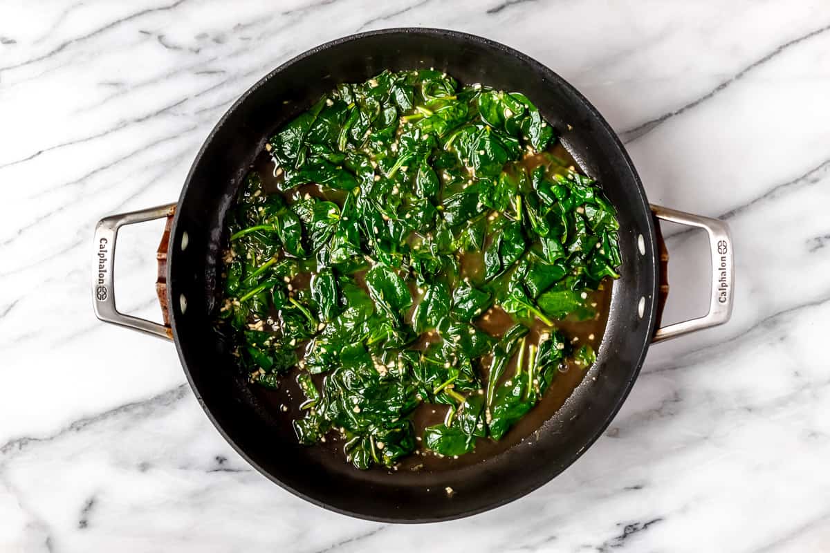 Cooked spinach and garlic in a black skillet.