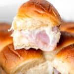 A single ham and cheese slider on top of the rest of the sliders in a white casserole dish with text overlay.