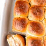 Ham and cheese sliders with one turned on its side in a white casserole dish with text overlay.