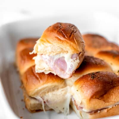 A single ham and cheese slider on top of the rest of the sliders in a white casserole dish.