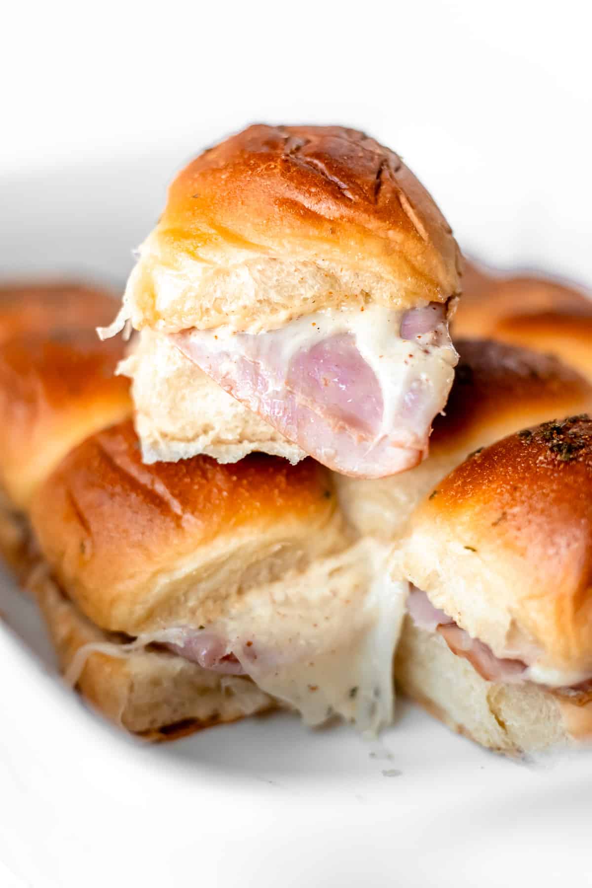 A single ham and cheese slider on top of the rest of the sliders in a white casserole dish.