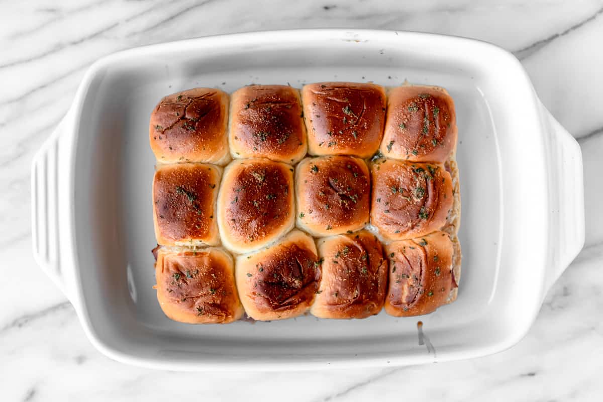 Overhead view of baked ham and cheese sliders in a white casserole dish over a marble background.