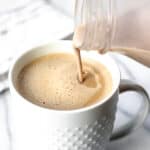 Irish cream coffee creamer being poured into a white mug of coffee on a marble background with text overlay.
