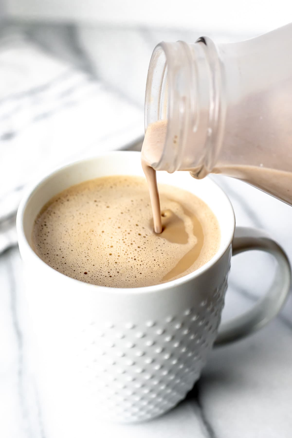 Irish cream coffee creamer being poured into a white mug of coffee on a marble background.