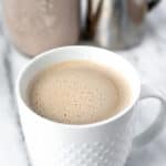 An Irish Latte in a white mug with a frothing pitcher and bottle of Irish cream coffee creamer in the background with text overlay.
