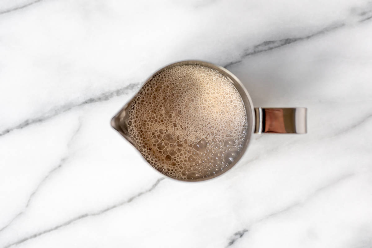 Frothed cream in a silver mug on a marble background.