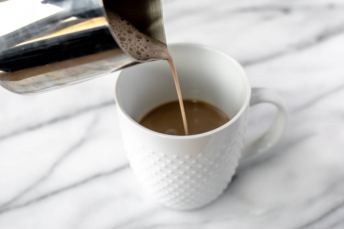 Frothed creamer being poured into a white mug of coffee and Irish cream liqueur.
