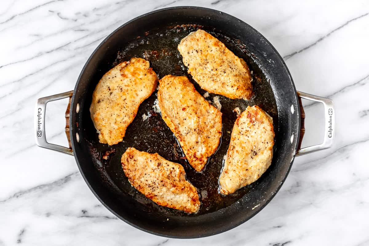 Five cooked chicken breasts in a black skillet.