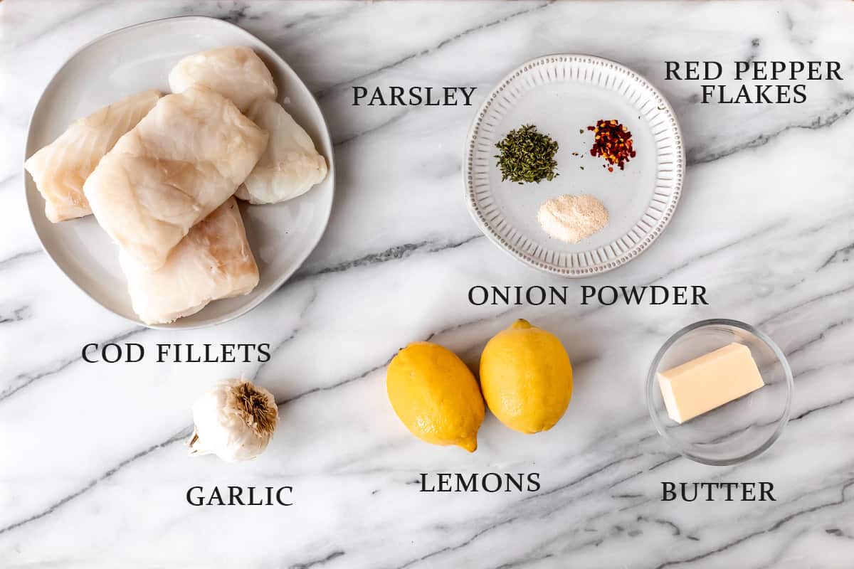 Ingredients needed to make baked lemon butter cod on a marble background with text overlay.