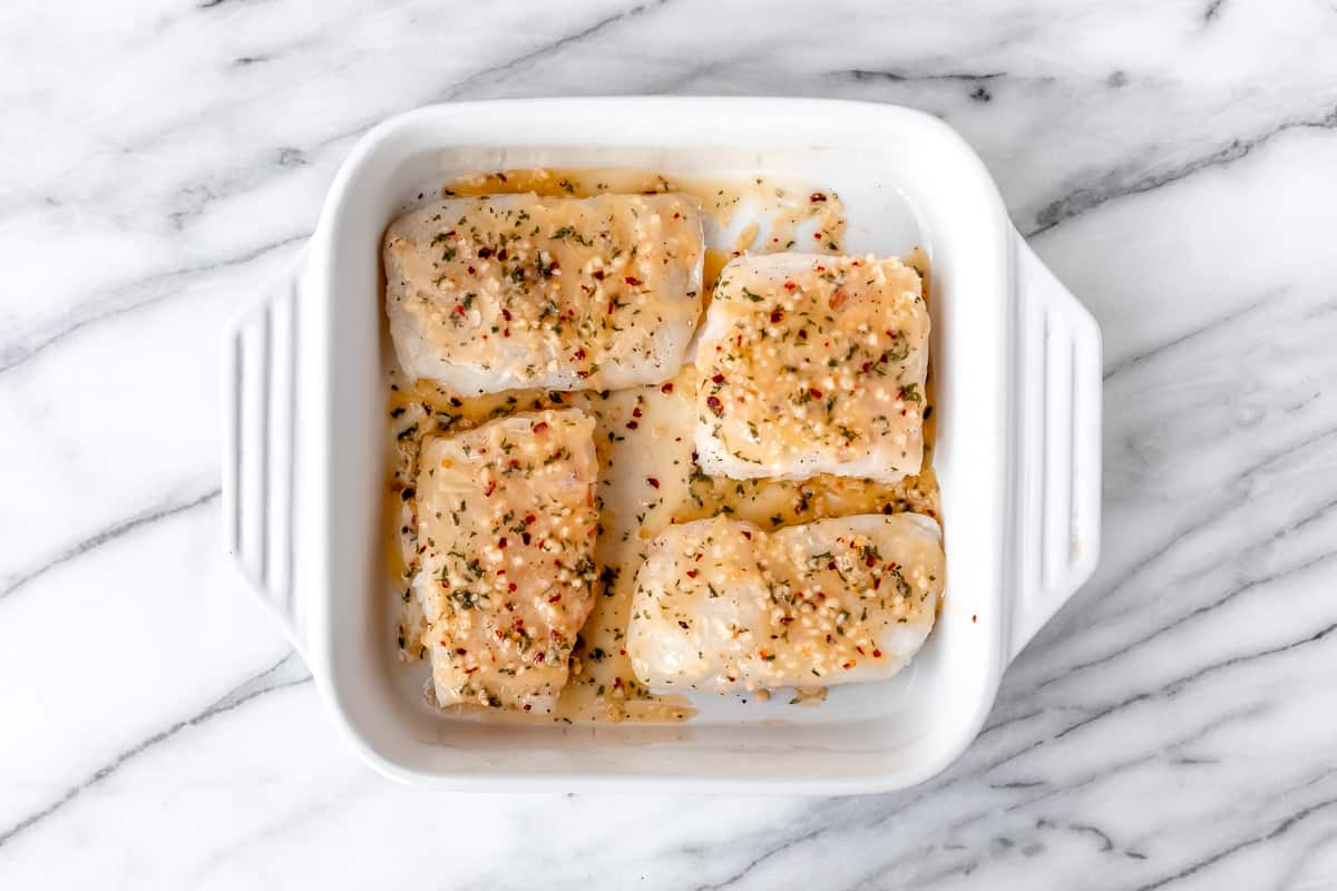 4 cod fillets topped with a lemon butter mixture in a white baking dish.