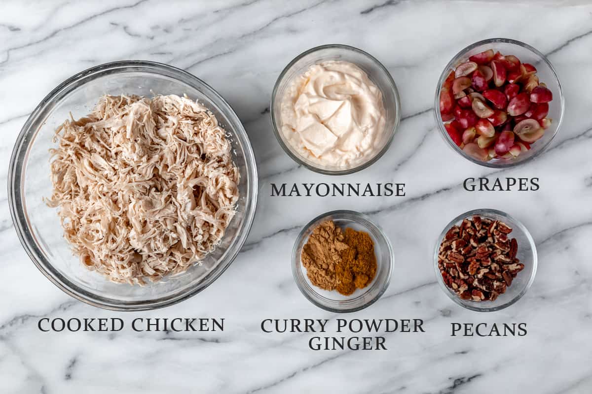 Ingredients needed to make curry chicken salad on a marble background with text overlay.