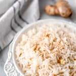 A white bowl of ginger rice with a knob of ginger and a blue and white towel in the background with text overlay.