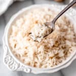 Ginger rice on a fork held up in front of a white bowl of rice.