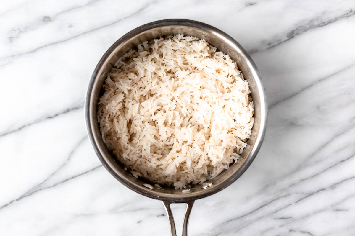 Cooked ginger rice in a silver pot over a marble background.