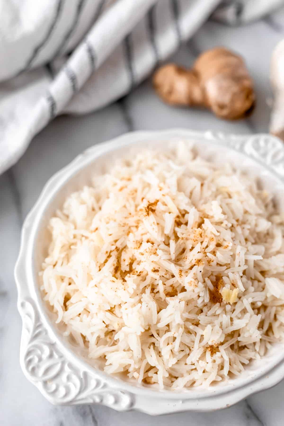 A white bowl of ginger rice with a knob of ginger and a blue and white towel in the background.