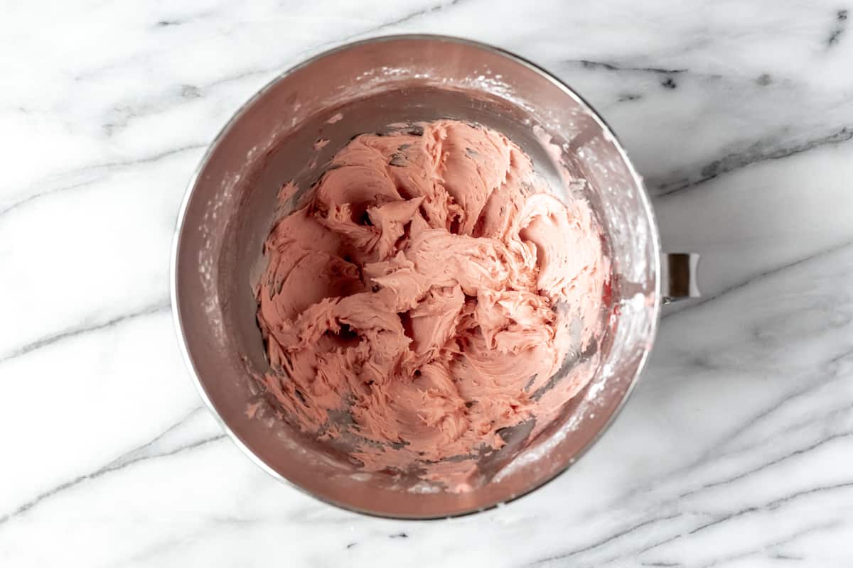 Strawberry buttercream frosting in a silver mixing bowl over a marble background.