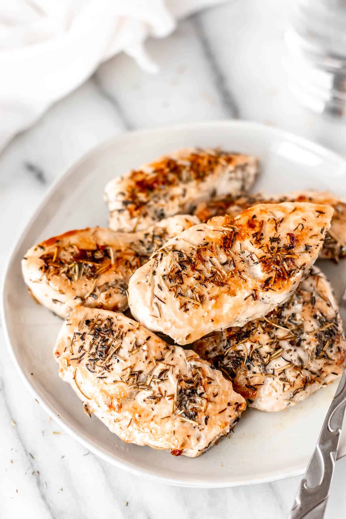 A white plate of pan seared turkey cutlets seasoned with rosemary and thyme.
