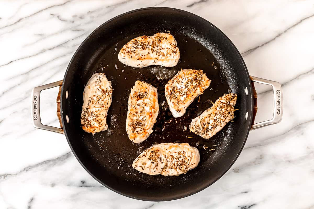 Herb seasoned turkey cutlets cooking in a black skillet.