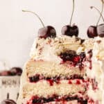 A white forest cake with a slice taken out to show the cherry juice and white chocolate inside.