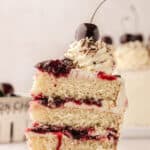 A single slice of white forest cake topped with fresh cherries on a white plate with the remaining cake in the background with text overlay.