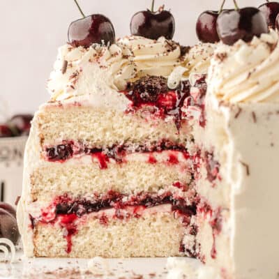 A white forest cake with a slice taken out to show the cherry juice and white chocolate inside.