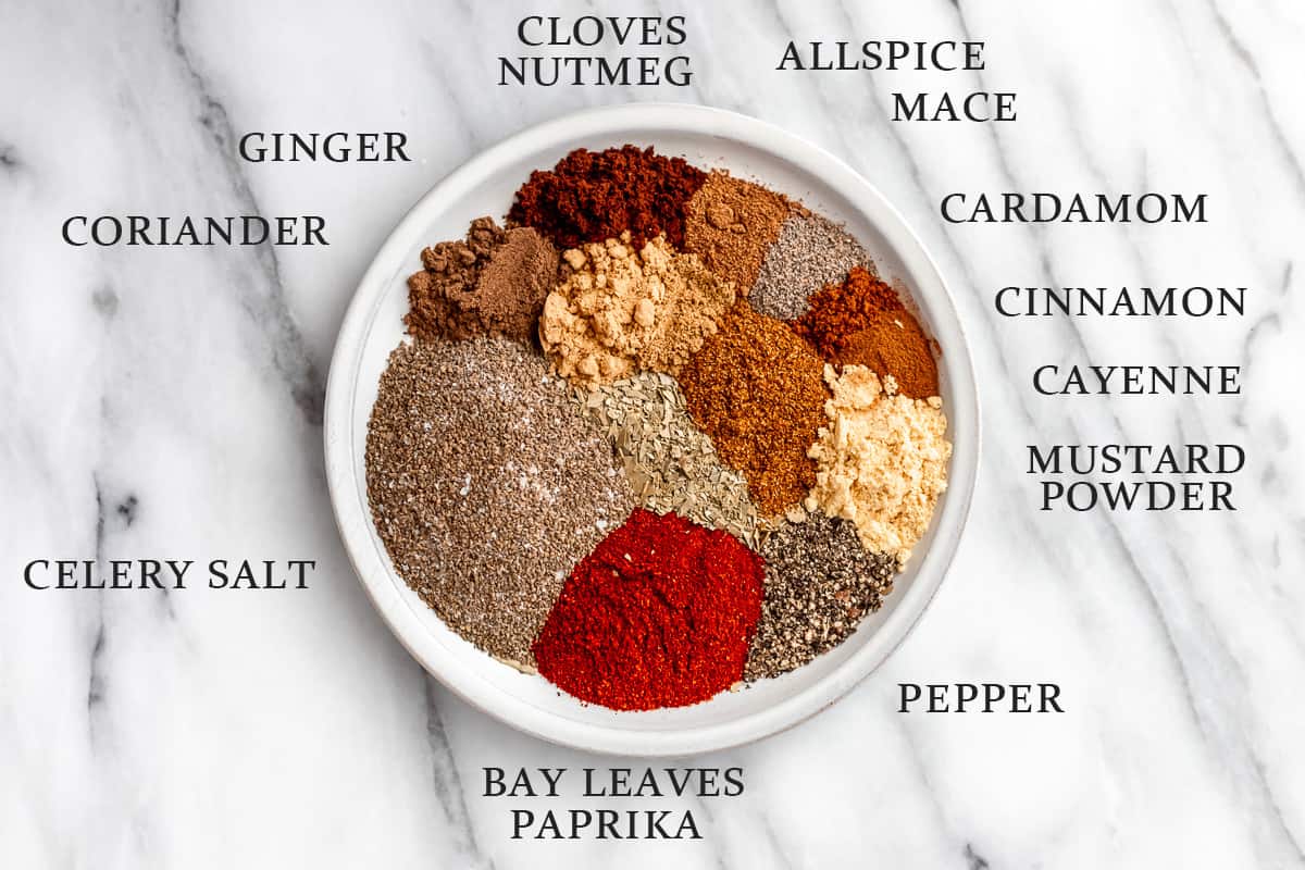 Ingredients needed to make homemade Old Bay Seasoning on a plate on marble background with text overlay.
