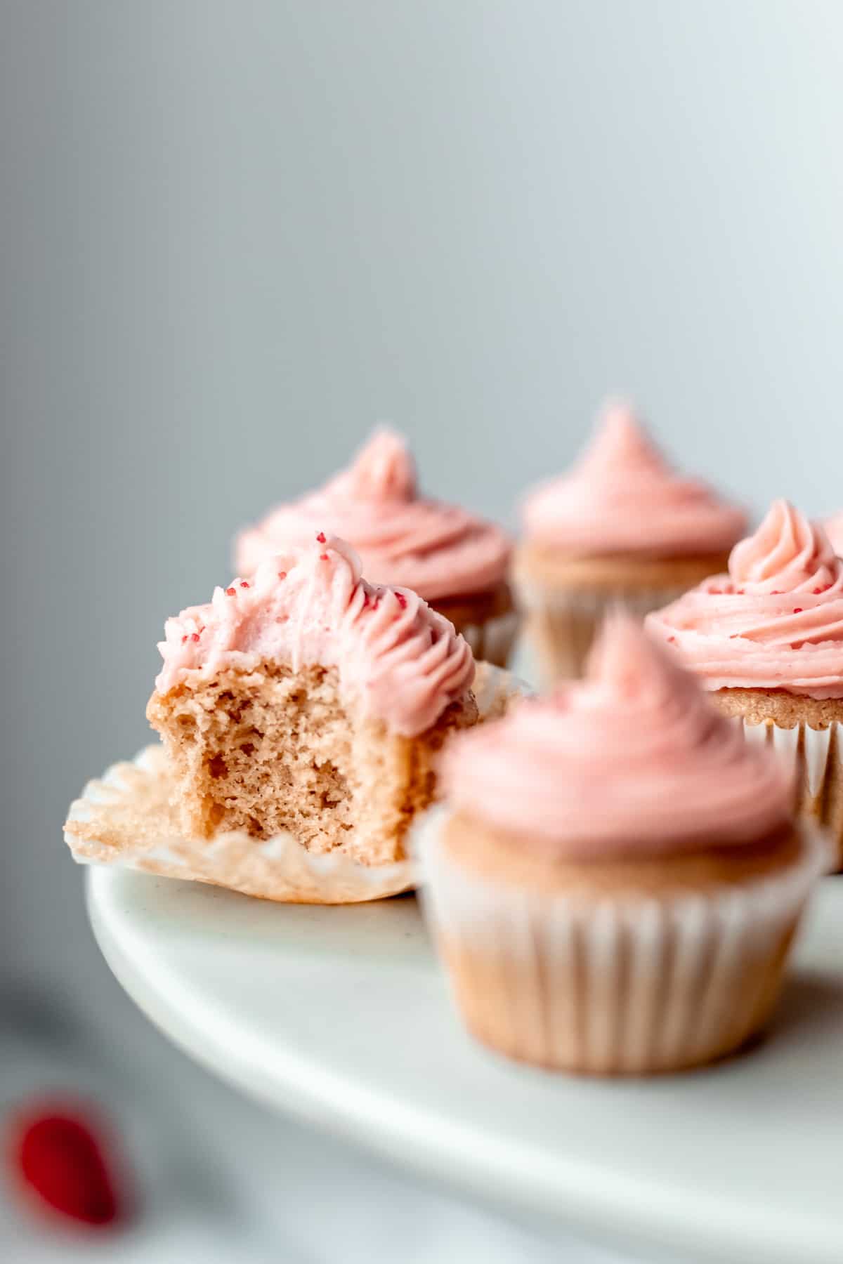 A mini strawberry cupcakes with a bite taken out of it with other mini cupcakes around it on a gray cake stand.