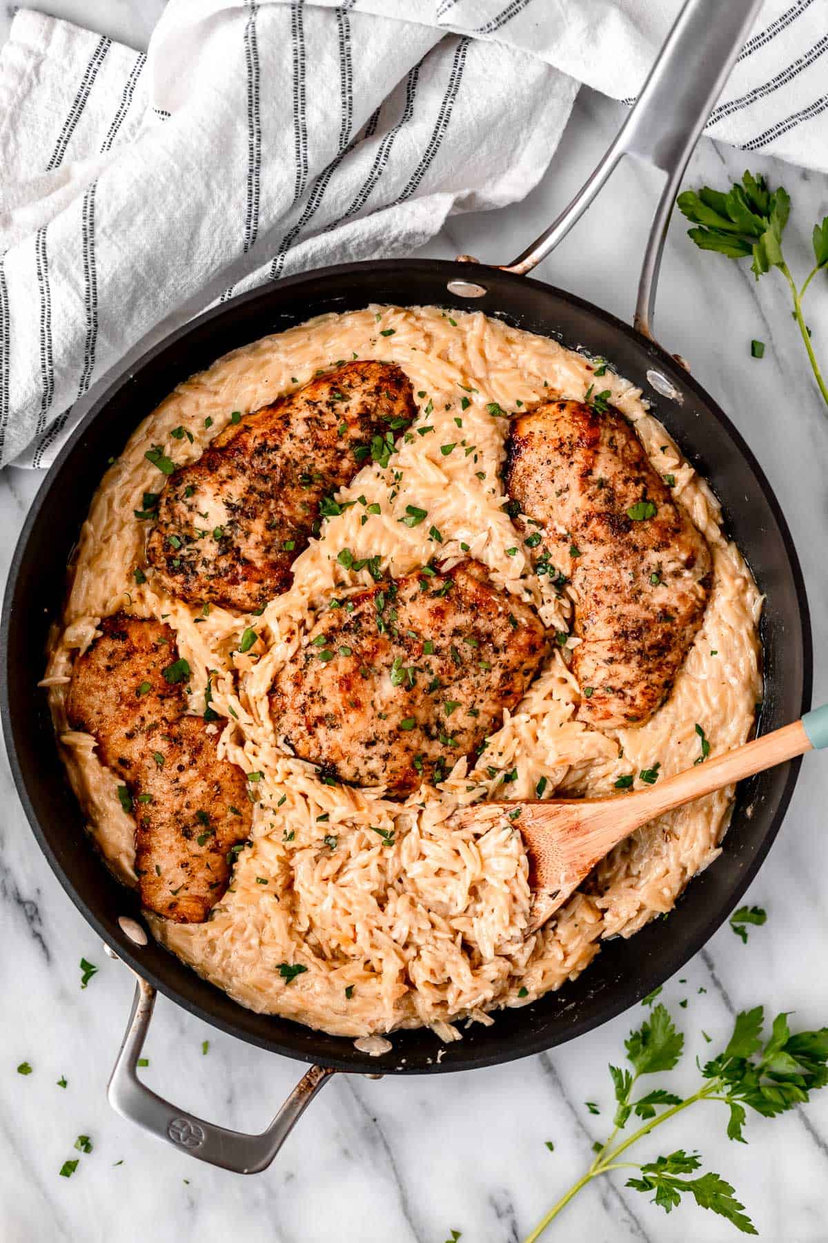 Parmesan Chicken Orzo in a skillet with a wood spoon lifting up some of the pasta.